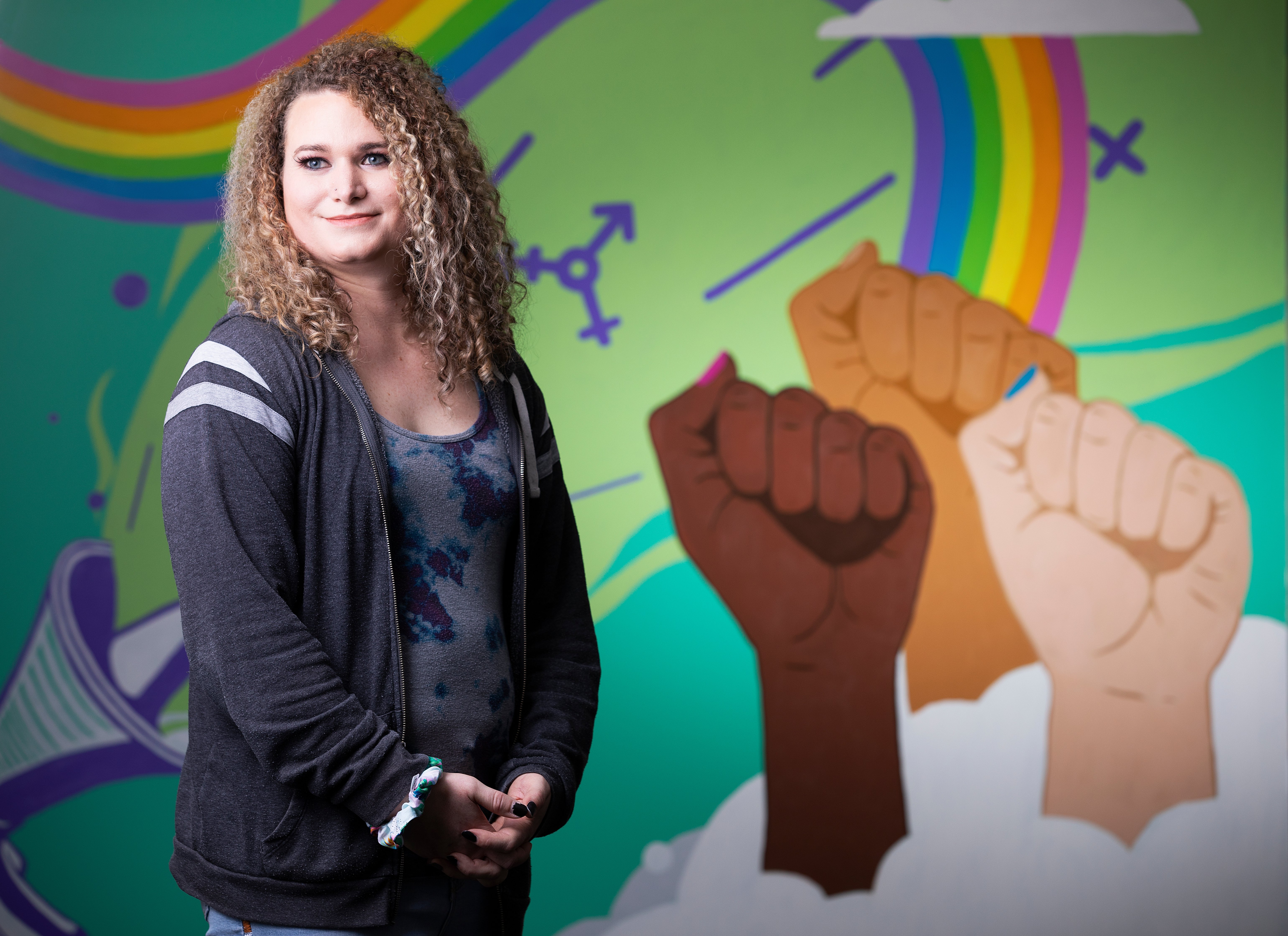 Photo of Ally Nelson behind a LGBTQIA+ mural."