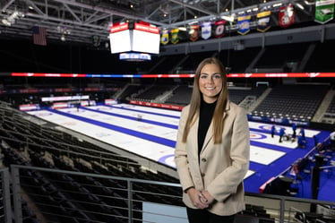 Photo of Ana Bellinghausen standing in front of the USA Olympic Curling trials ice. 