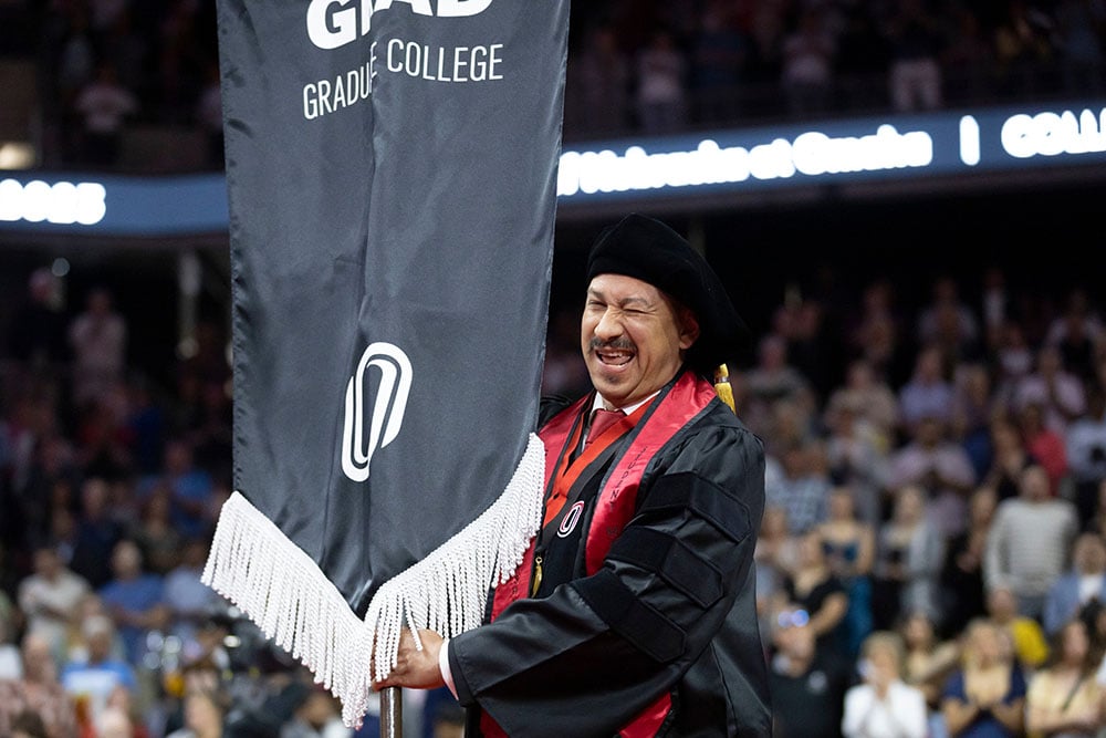 UNO doctoral public administration student Felipe Blanco winks at the camera while carrying the student marshal flag during the 2023 May Commencement ceremony.